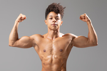 Wall Mural - A young Brazilian man stands confidently with flexed arms, highlighting his muscular build. He emphasizes an athletic lifestyle and commitment to fitness, isolated against a neutral background.