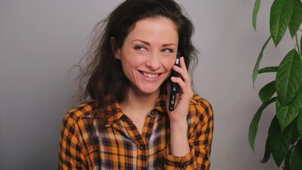 Sticker - Happy laughing and smiling woman talking on mobile phone at home near the green frower in bright orange style shirt and texting on the screen to buy online. Closeup natural positive expression video	
