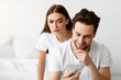 © Prostock-studio - Jealousy. Suspicious Wife Reading Husband's Messages On Smartphone Standing Behind His Back While He Texting In Social Media Indoors. Jealous Girlfriend Checking Boyfriend's Chats Suspecting Affair