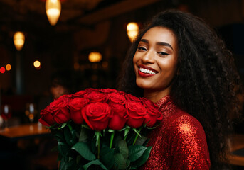 Wall Mural - happy young smiling african woman holding red rose bouquet