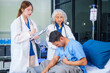 © NanSan - Two female doctors examine a patient lying on a hospital bed,discuss the medical chart,administer medicine,and provide encouragement, ensuring compassionate care and fostering the patient's recovery