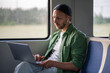 © DimaBerlin - Focused businessman type on laptop, wearing earphones while traveling by train to work. Mobile office setup, digital nomad lifestyle, remote workspace, tech savvy freelancer, commute with productivity