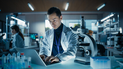 Leinwandbilder - Portrait of a Young Graduate Student Working in a Laboratory, Using Advanced Microscope, Writing Down Research Data on a Computer. Multiethnic Biotechnology Specialist Using Modern Tools