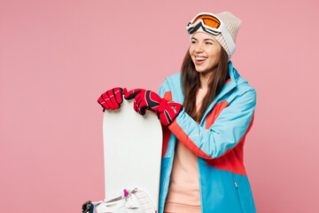 Poster - Snowboarder young woman in warm blue padded jacket ski goggles mask spend extreme weekend winter season in mountains hold snowboard look aside on area isolated on plain pink background Hobby concept