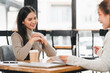 © kenchiro168 - Two women having friendly conversation at wooden table in modern cafe, with coffee cup and documents on table, creating professional yet relaxed