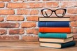 © Somporn - Studying at homestacked books and glasses against a brick wall educational content cozy environment close-up view