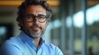 © imagineRbc - A man with glasses and a beard is smiling at the camera. He is wearing a blue shirt and a blue tie