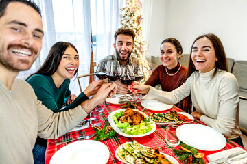 Group of young people taking selfie while sitting at the table - Happy family toasting red wine glasses at christmas fest - Winter holiday xmas concept with friends eating together at home party