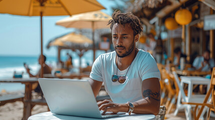 Wall Mural - A cheerful young professional handsome man wearing t-shirt and shorts, he is looking at a sleek laptop at a small beachside cafe.