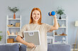 © Studio Romantic - Happy fit young red-haired girl, woman smiling looking at camera holding scales and using dumbbells, wearing sportswear at home, sport youth portrait planning active life and starts losing weight