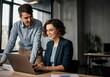 © stock.metket.com - Happy businesswoman wearing eyeglasses working on laptop with coworker in office