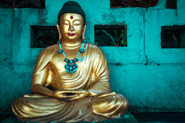 Serene golden Buddha statue adorned with turquoise and beaded jewelry, set against a weathered teal backdrop, symbolizing peace and spirituality.