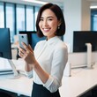 © Hardikbhai bhamani - Cheerful beautiful Asian woman holding smartphone in the office workplace,