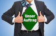 © Robert Kneschke - Geschäftsmann im Anzug zeigt Slogan „Unser Auftrag“ unter seinem Hemd