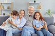 © Studio Romantic - Portrait of a happy grandparents sitting on sofa with their grandchildren boy and girl in the living room at home looking at camera and smiling. Kids enjoying leisure time with grandma and grandpa.