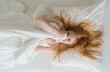 © ullision - Sexy redhead woman with flowing red hair lies in a cozy white bed, playfully hiding her face with the blanket. The soft lighting and serene atmosphere convey warmth and comfort