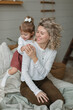 © RooM The Agency - Smiling Woman kneeling on a bed with her young daughter jumping onto her back