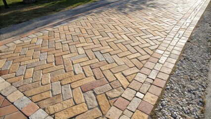 Leinwandbilder - A herringbone pattern of brick pavers create a pathway bordered by a row of stones and a strip of grass.