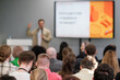 © Anton Gvozdikov - Professional speaking at conference room engaging audience with presentation. Focus on screen and speaker.