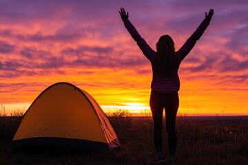 Fototapete - A silhouetted figure celebrates a vibrant sunset near a camping tent.