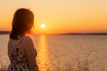 Canvas Print - Woman standing in front of lake at sunset. Girl in blue sky at sunset. A sunset over the river and nature. A girl in a blue dress and blue skirt and a blue sky at lifestyle sunset in nature.