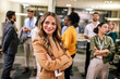 © Mediteraneo - Business woman standing in her office in front of her colleagues with her hands crossed.