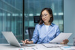 © Liubomir - Asian woman businesswoman engaged in work at her desk, using a laptop and reviewing documents. The office setting highlights productivity and professionalism, reflecting a focused and organized work