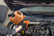 © AnastasiiaAkh - Mechanic in gloves pouring motor oil into a car engine using an orange funnel, in a workshop. Concept of vehicle maintenance
