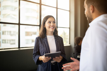 Leinwandbilder - Two professionals are interacting in a bright office space. One person is holding a tablet, while the other is speaking animatedly. Their teamwork reflects a commitment to success and diversity.