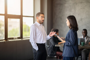 Leinwandbilder - Two professionals engage in a discussion in a contemporary office. The atmosphere reflects teamwork and cooperation, with diverse individuals working together towards success.
