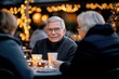 © Milos - A cheerful elderly man enjoys a delightful moment with friends at an outdoor gathering, radiating warmth and happiness amid festive lights, celebrating life's beautiful moments.