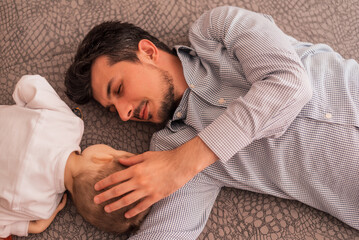 Wall Mural - A young father shares love with his son and spends time together at home, lying on the bed, top view.