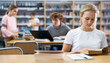 © JackF - Portrait of a fifteen-year-old schoolgirl sitting at a desk in the school library, attentive reading a book