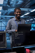 © DC Studio - Smiling engineer pleased by recovery plan, monitoring data center energy consumption. Happy african american employee in server room making sure sensors are functioning optimally, doing disk checks