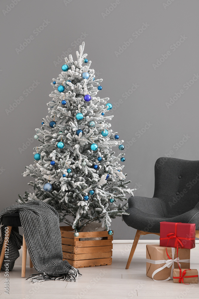 Beautiful Christmas tree with gift boxes and armchair near grey wall