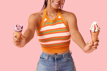 Poster - Young African-American woman with sweet ice-cream in waffle cones on pink background