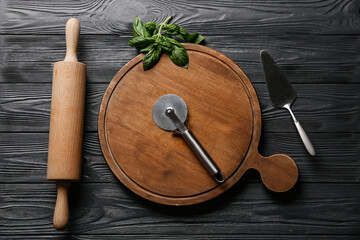 Canvas Print - Board with stainless steel pizza cutter, spatula and rolling pin on dark wooden background