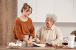 © Pixel-Shot - Young woman and her grandmother cooking pie with baking dish at table in kitchen