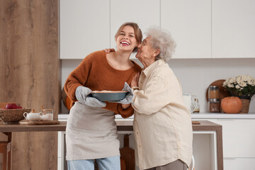 Sticker - Senior woman kissing her granddaughter with tasty pie in kitchen