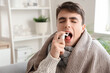 © Pixel-Shot - Ill young man with plaid spraying his sore throat at home, closeup