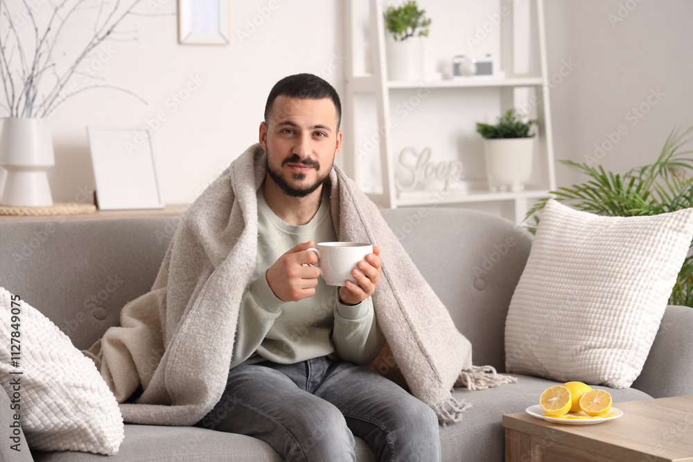 Ill young man with plaid and lemon tea sitting on sofa at home