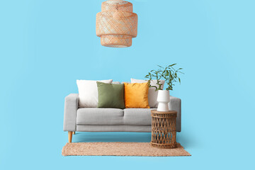 Canvas Print - Table with bamboo stems in vase, grey sofa, rug and lamp on blue background