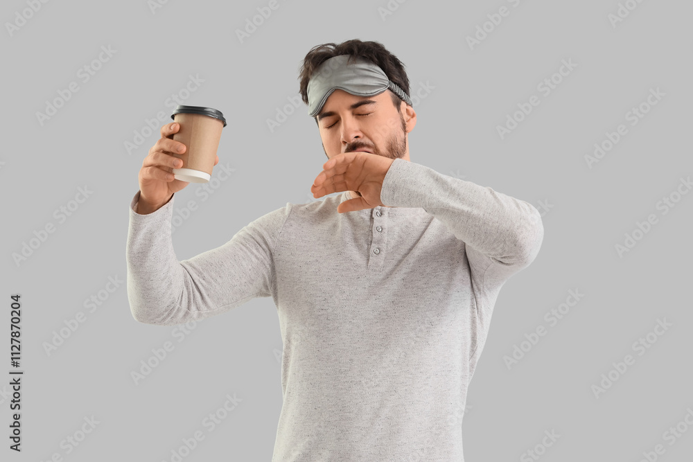 Sleepy young man with coffee cup yawning on light background
