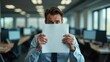 © 18042011 - Businessman holding blank paper, looking shy in open plan office