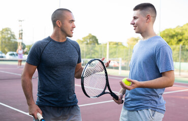 Wall Mural - Friendly teenage boy and adult man chatting on outdoor tennis court.