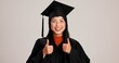 © Nina2024/peopleimages.com - Thumbs up, graduation and smile with portrait of asian woman in studio for success, college degree or award. Achievement, education and university student with person on white background for mockup