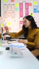 Female ui ux designer working on mobile app design prototype. Ui/ux designer is analyzing the user flow of a mobile application prototype she is designing, using sticky notes on a whiteboard.