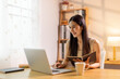 © David - Drinking coffee, asian woman working on laptop at home office desk, copy space