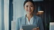 © Julia - Happy young Asian saleswoman looking at camera welcoming client. Smiling woman executive manager, secretary offering professional business services holding digital tablet standing in office.