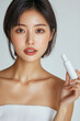© Itsaya - confident woman in her 30s holds skincare product, showcasing clear skin and serene expression in studio setting